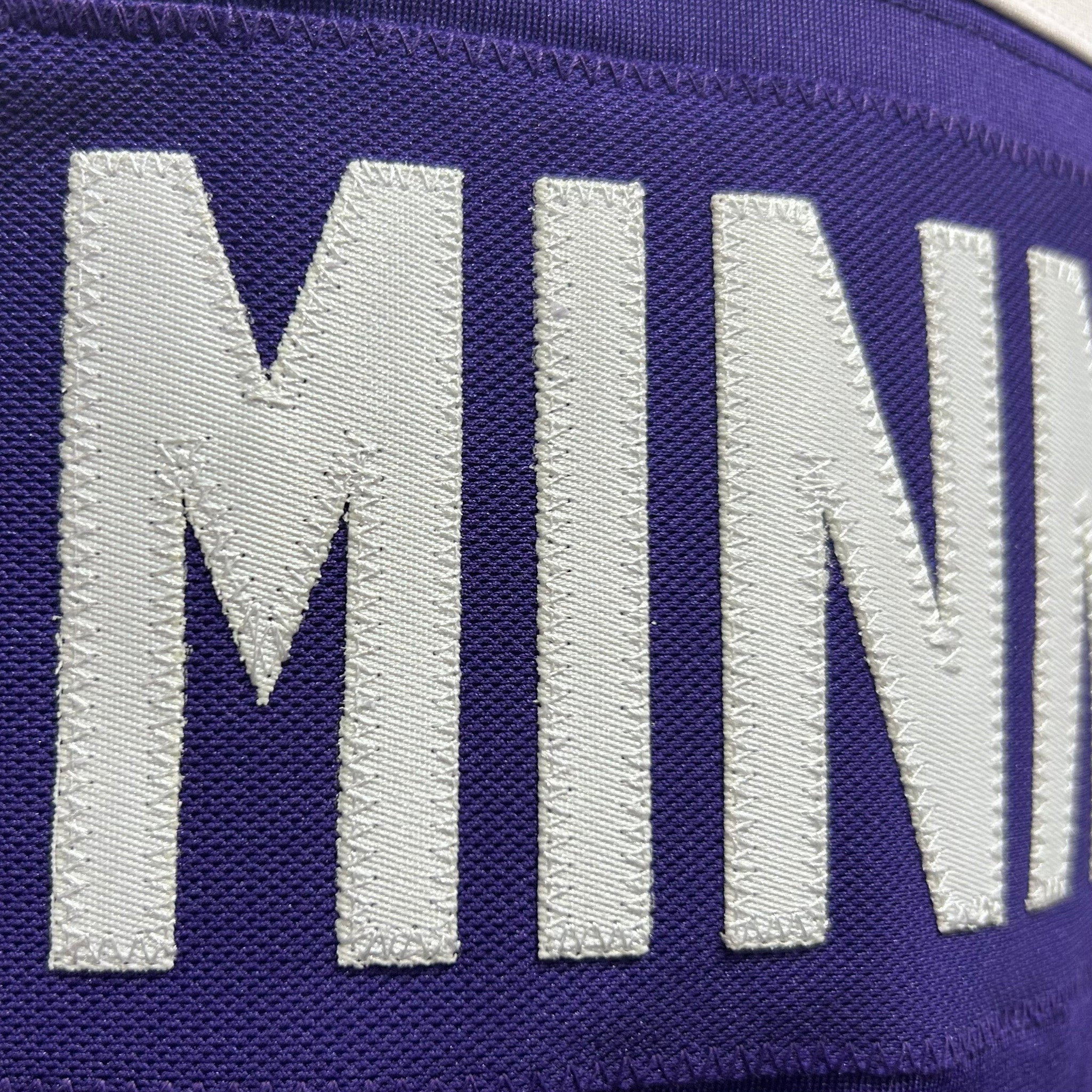 Close-up of a purple fabric with white embroidered letters spelling 'MINNESOTA'.