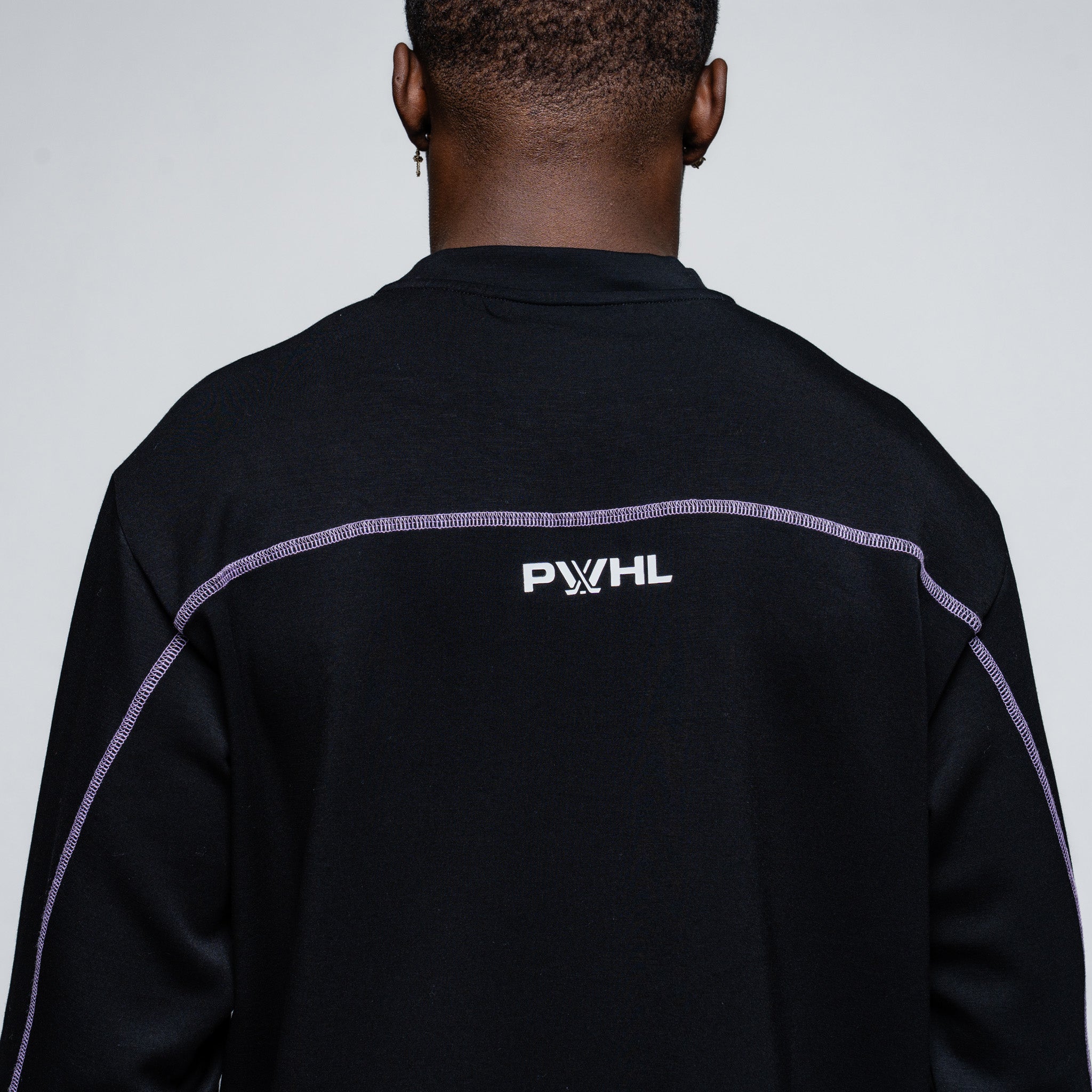 Person wearing a black sweater with 'PWHL' logo on the back against a gray background