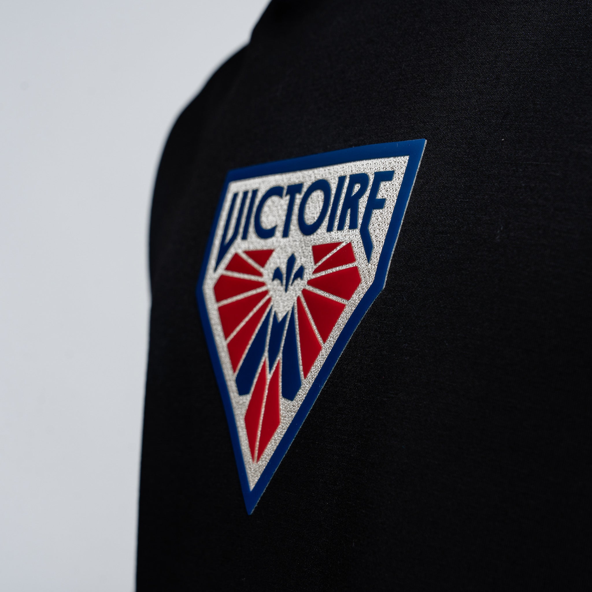 Black sweater with a 'Victoire' logo patch on a gray background