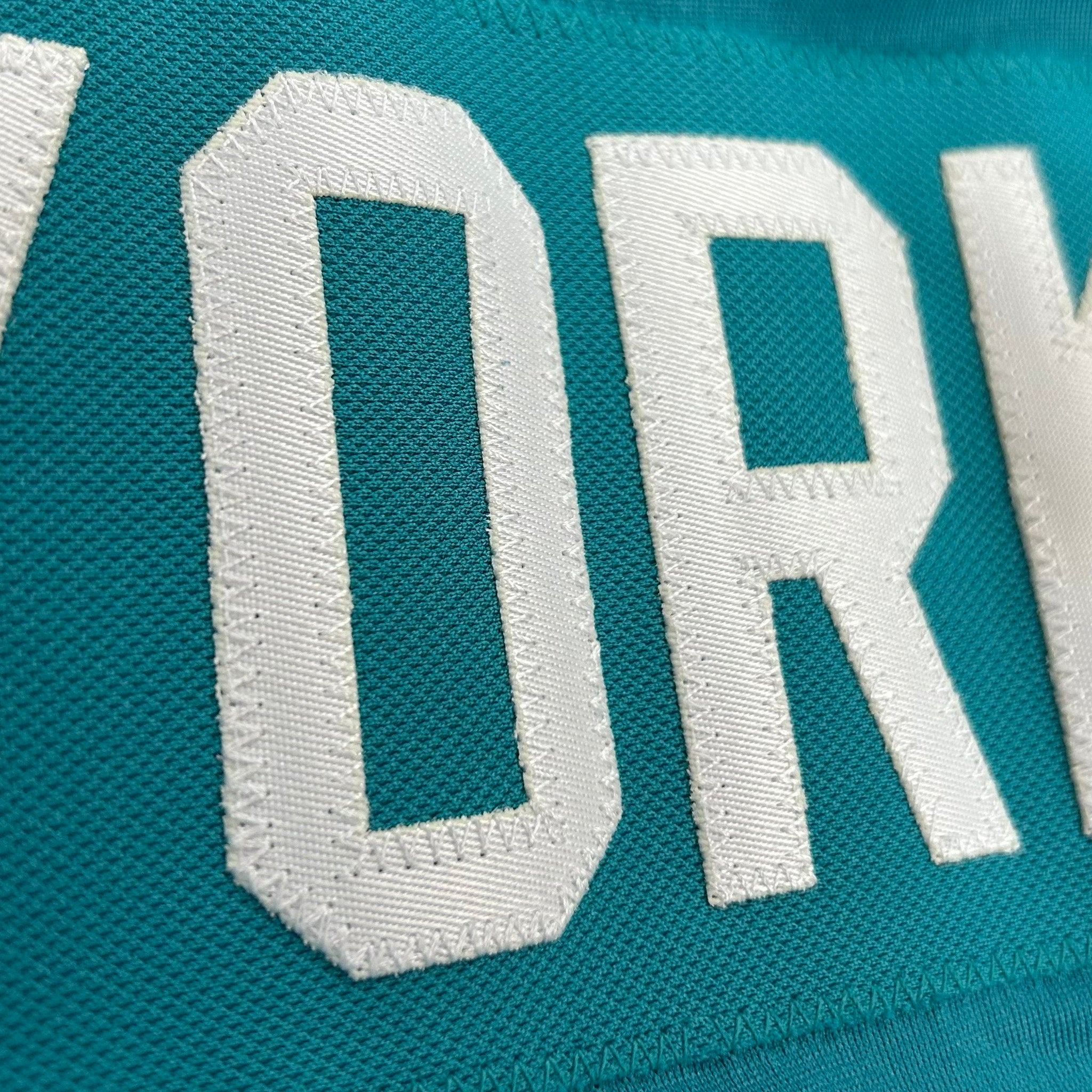 Teal fabric with white embroidered text on a textured background