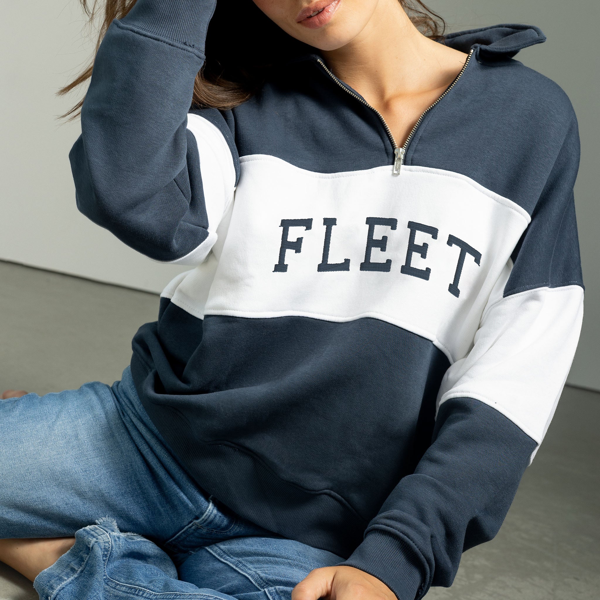 Person wearing a navy and white hoodie with 'FLEET' text, sitting on a gray floor.