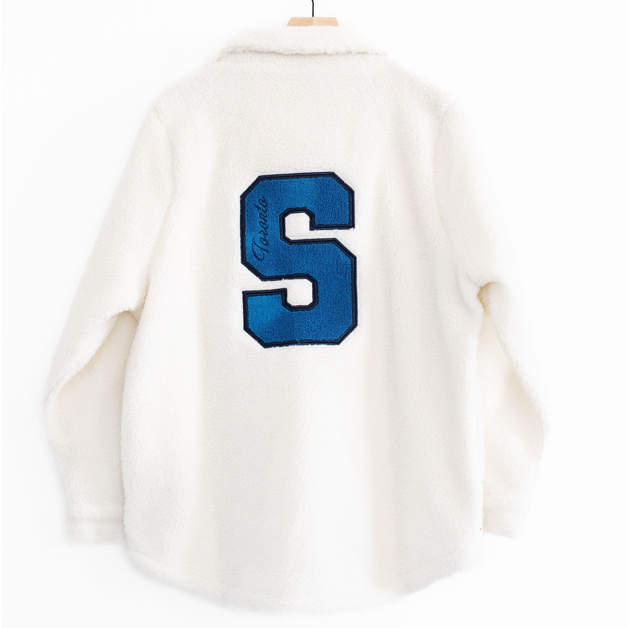 The back of a White Sherpa Jacket with a Blue S that says Toronto inside it