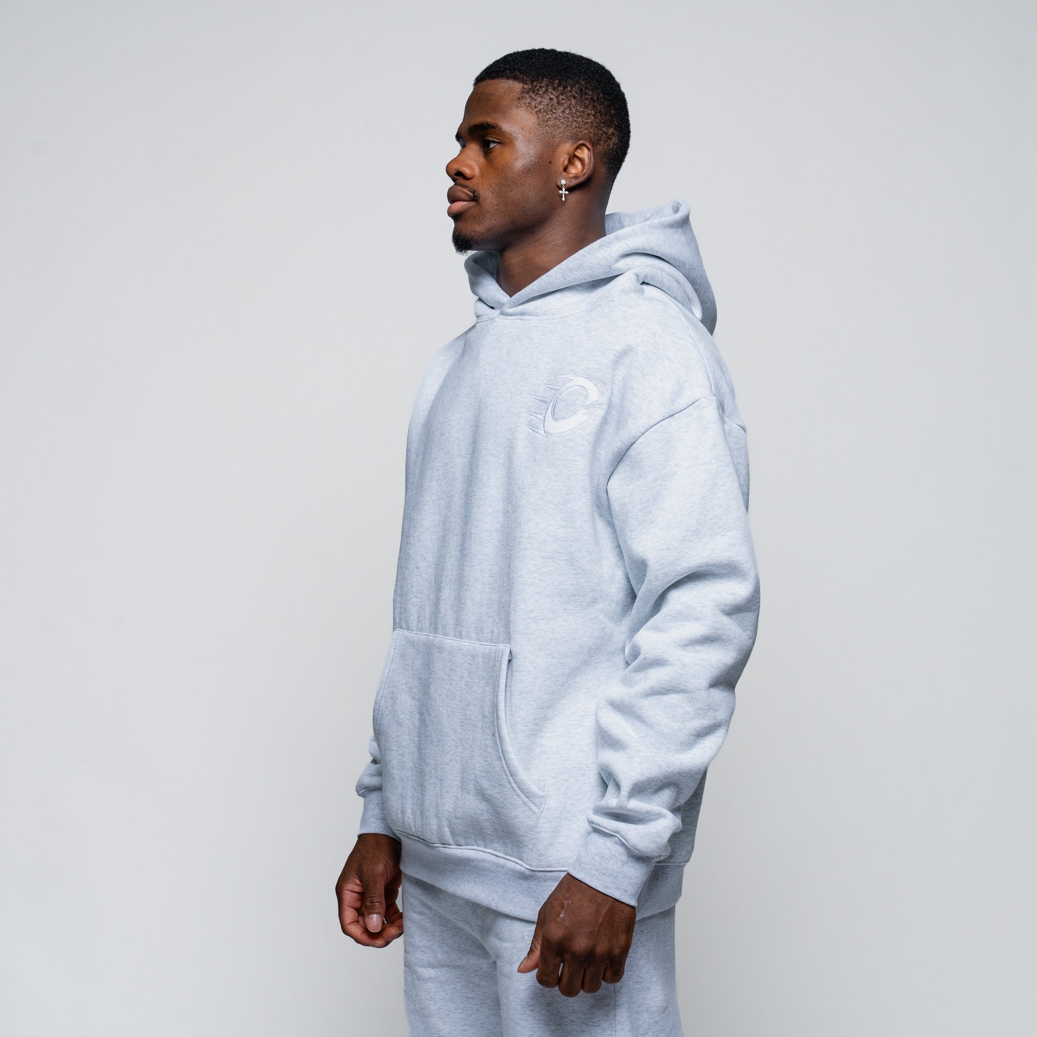 Man wearing a light gray hoodie and pants on a plain background