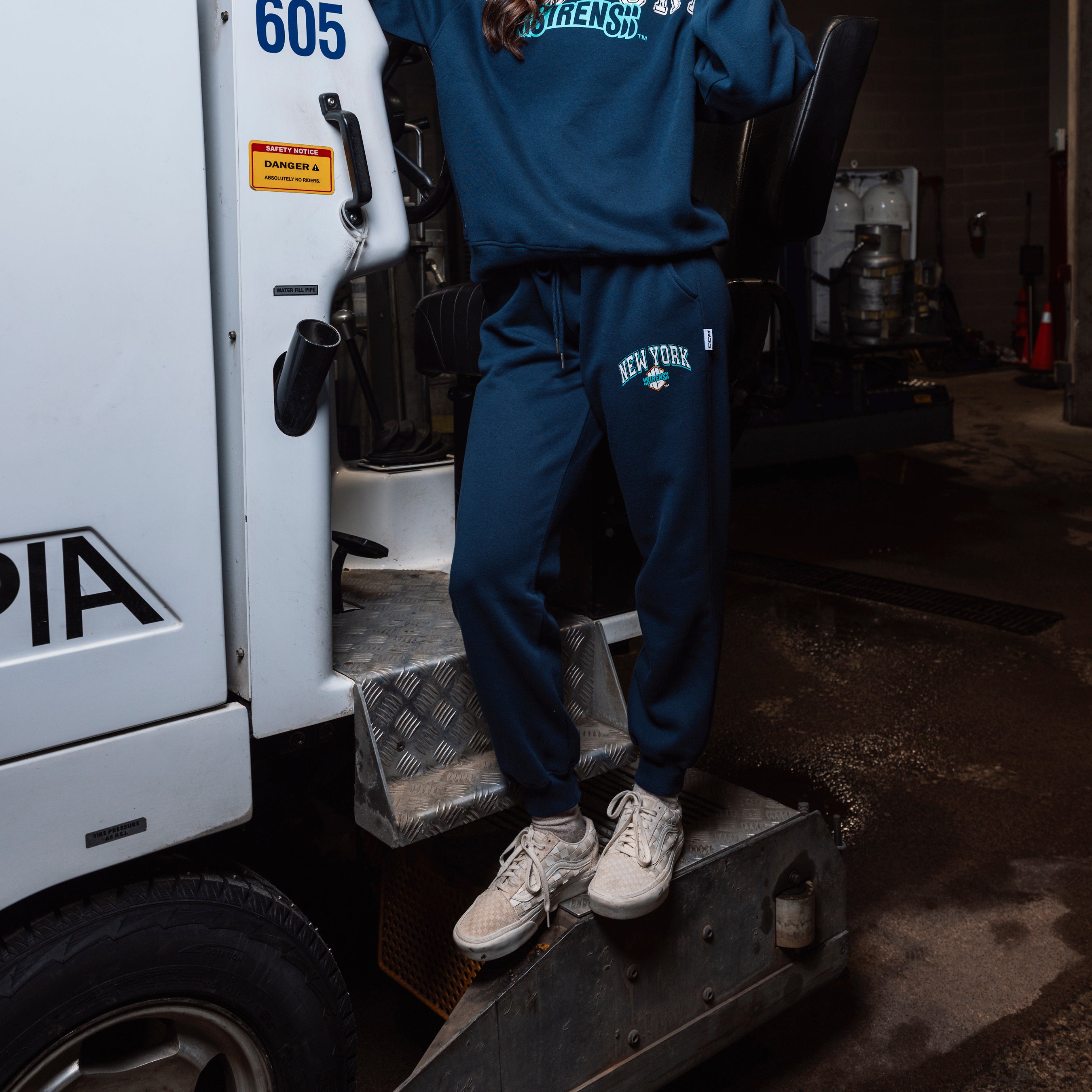 Person wearing a blue tracksuit with 'New York' text, standing on a vehicle step.
