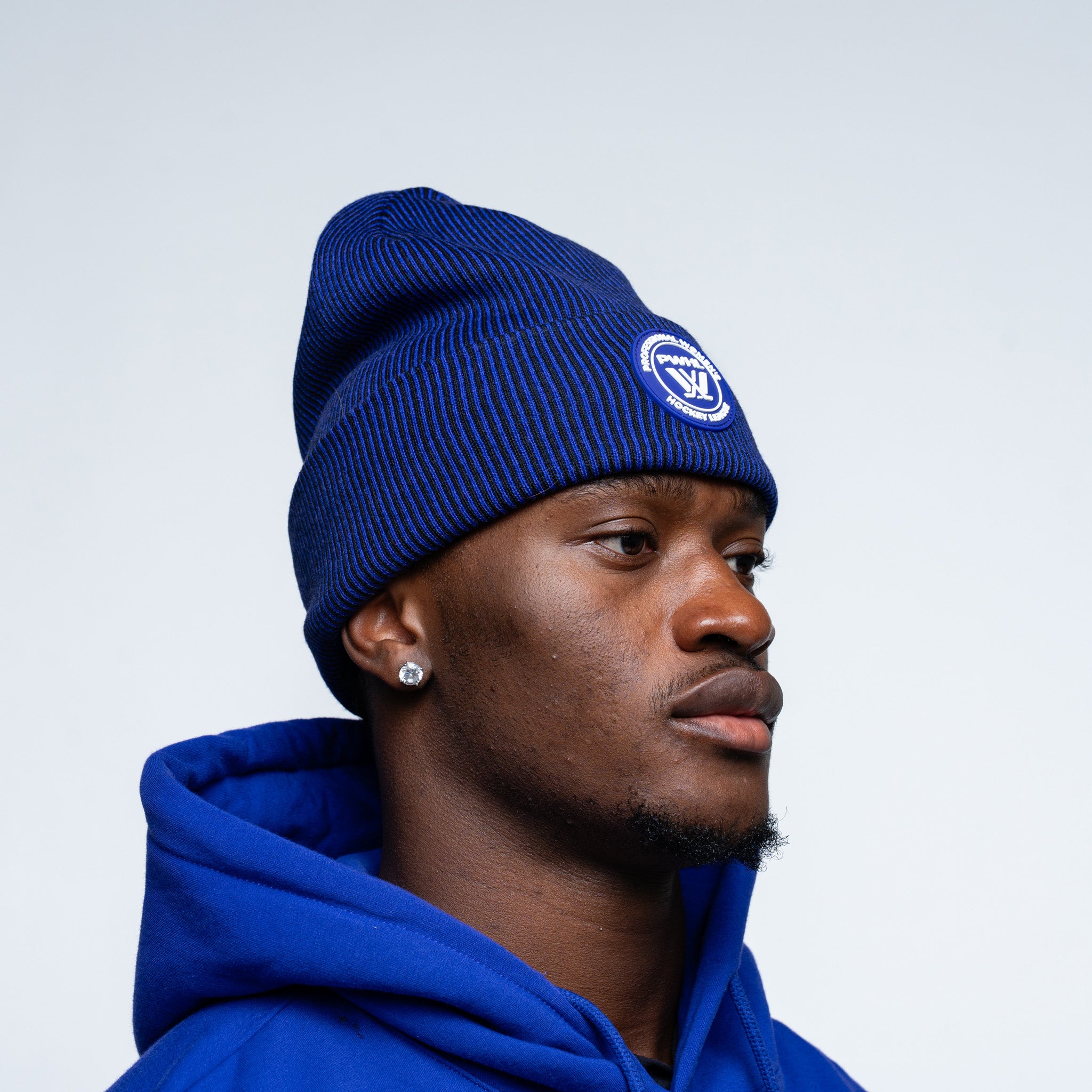 Person wearing a purple beanie and hoodie with a logo on a light gray background