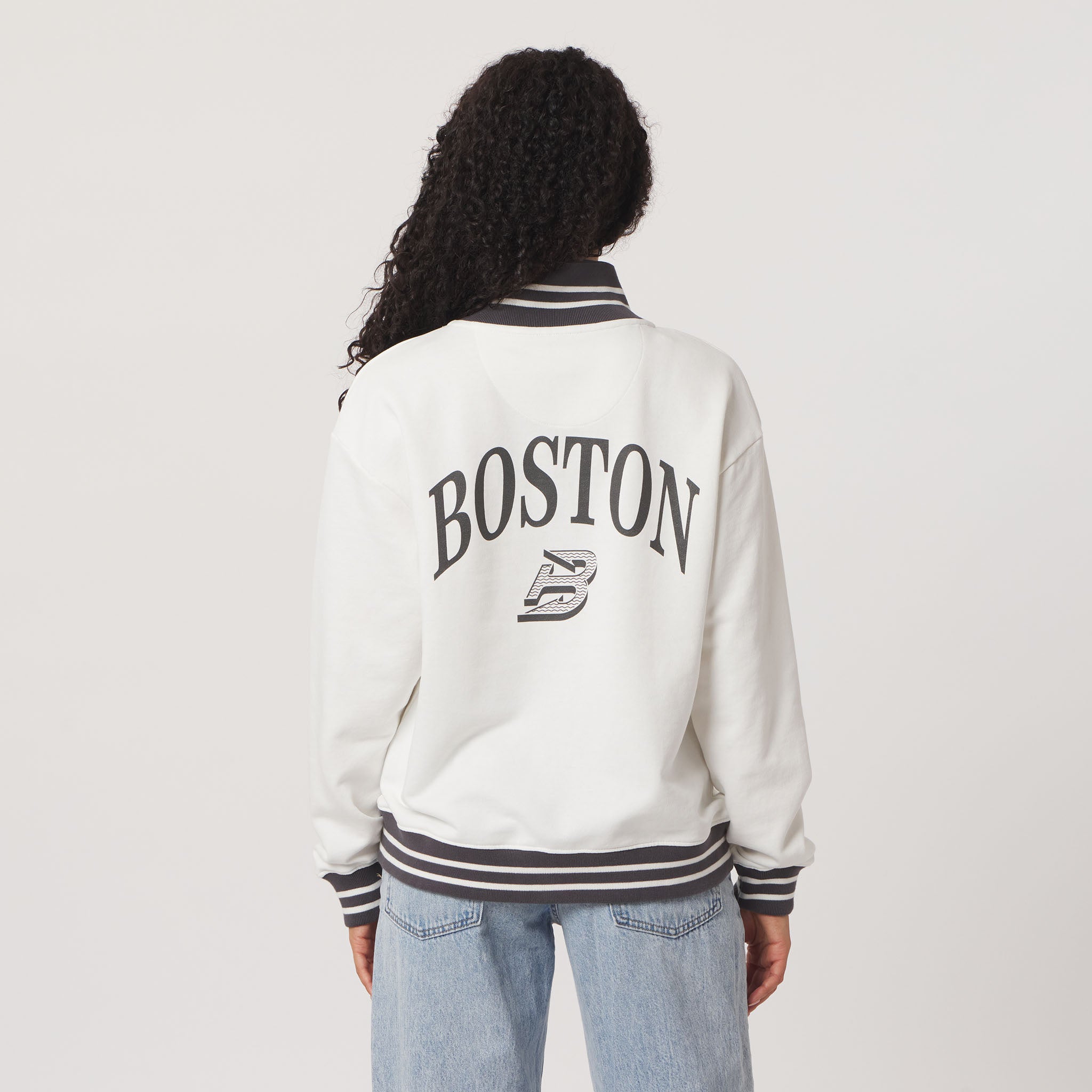 Person wearing a white letterman jacket with 'Boston' and a logo on the back, standing against a plain background.