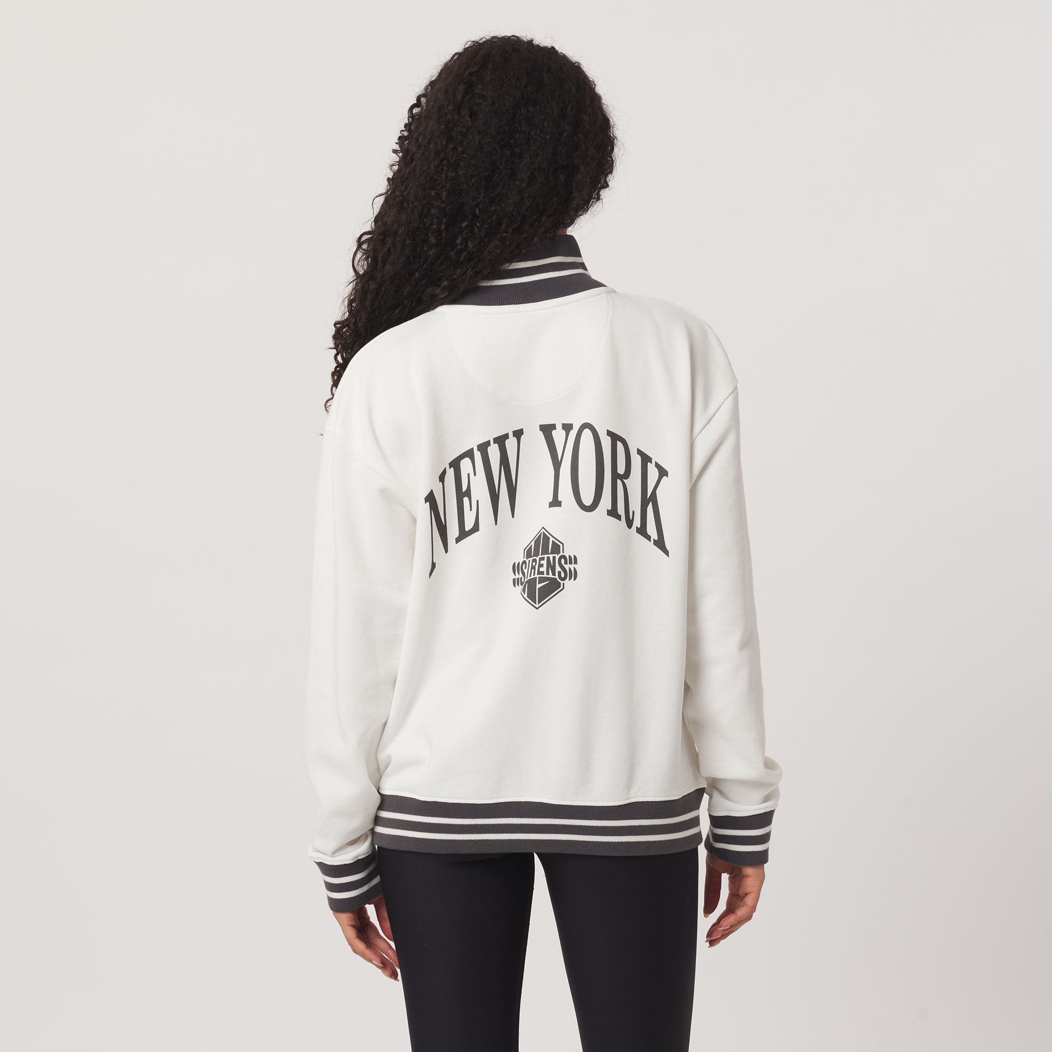 Person wearing a white 'New York' varsity jacket on a plain background