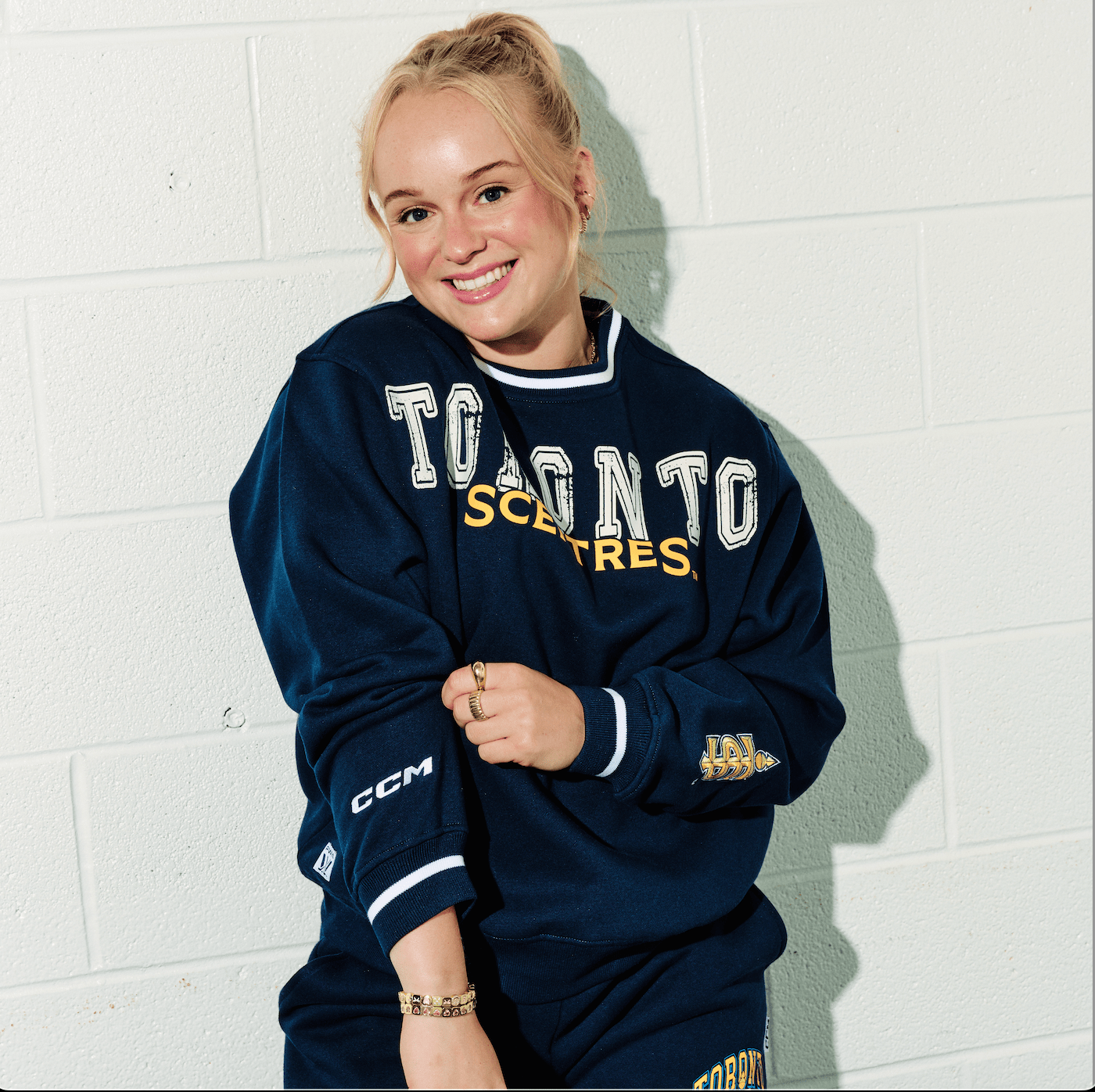 Person wearing a navy blue sports sweatshirt with visible branding against a white tiled wall.