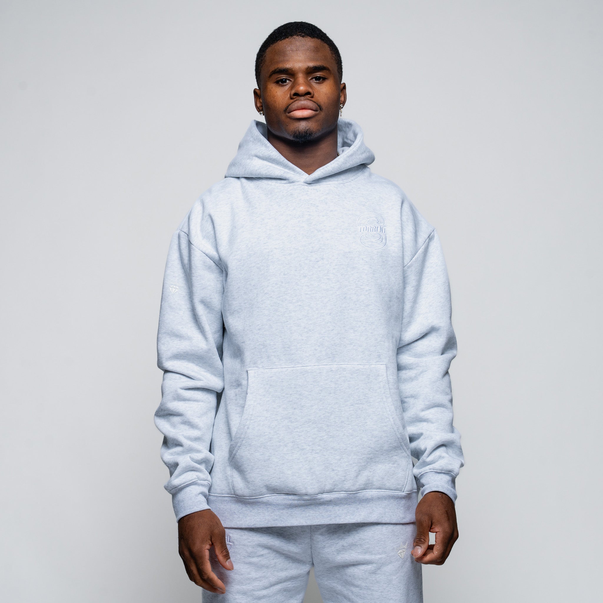 Man wearing a light gray hoodie and pants against a plain background