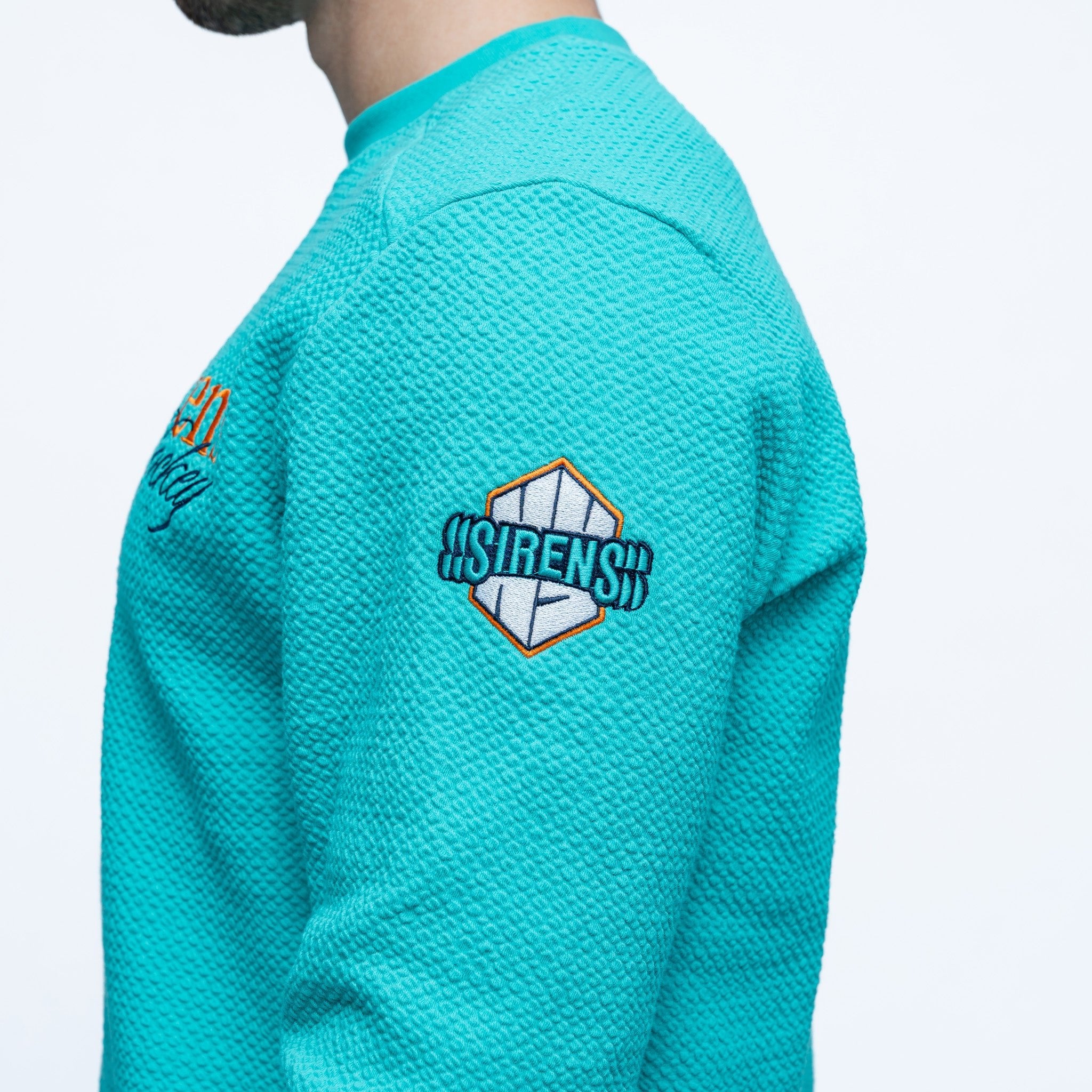 Teal sweatshirt with a logo on the sleeve against a white background