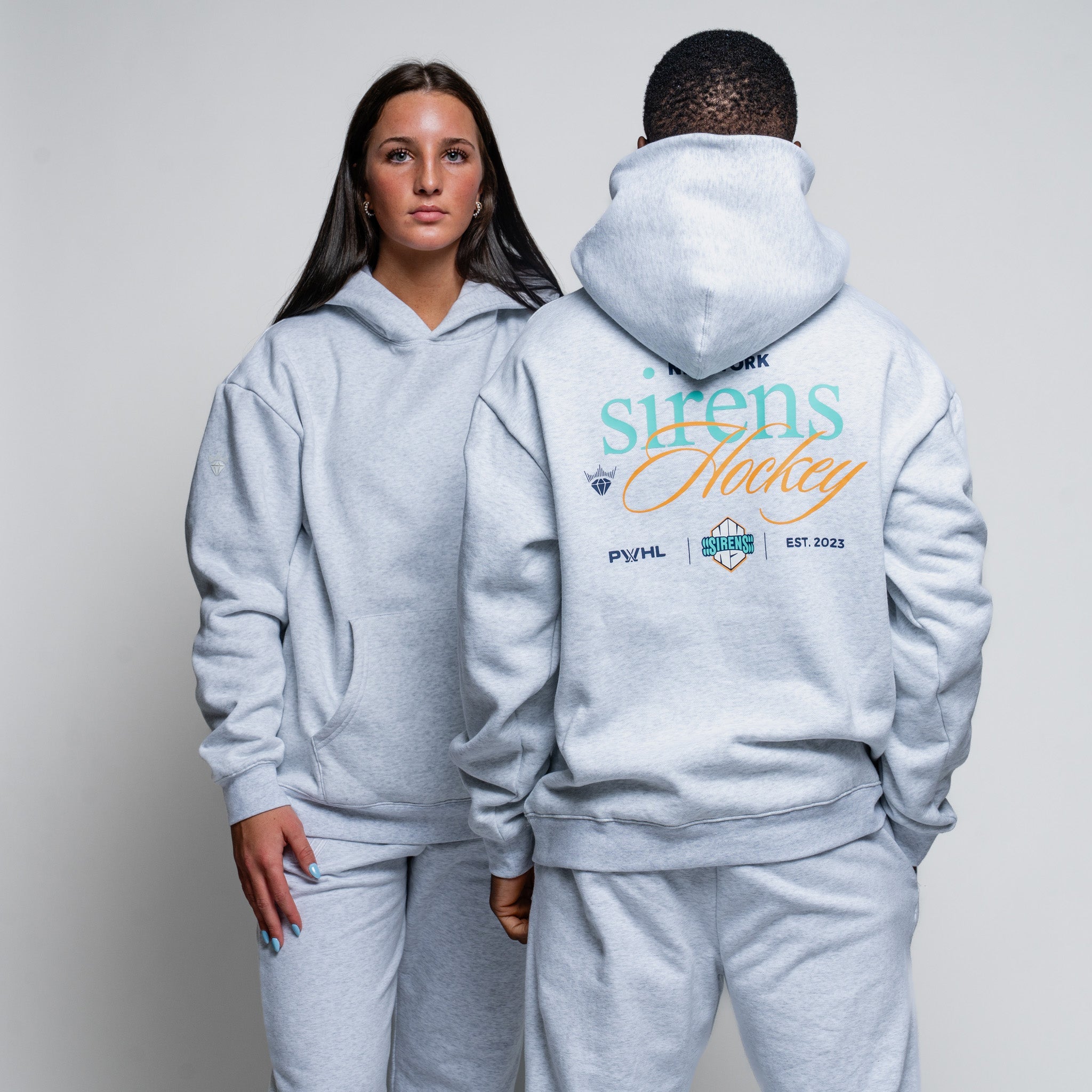 Two people wearing matching gray hoodies with 'sirens hockey' text on a plain background