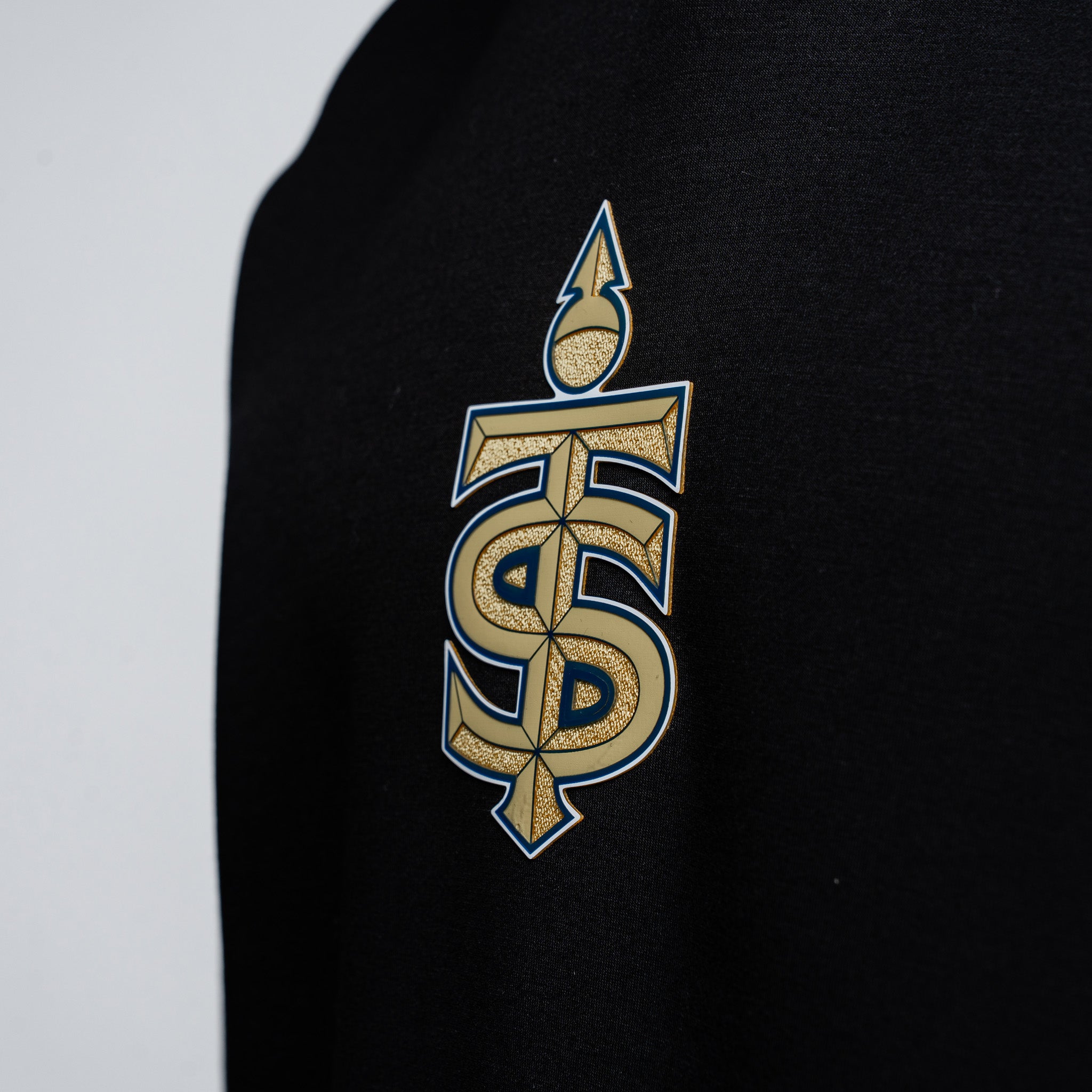 Black sweatshirt with a gold and blue logo on a light gray background