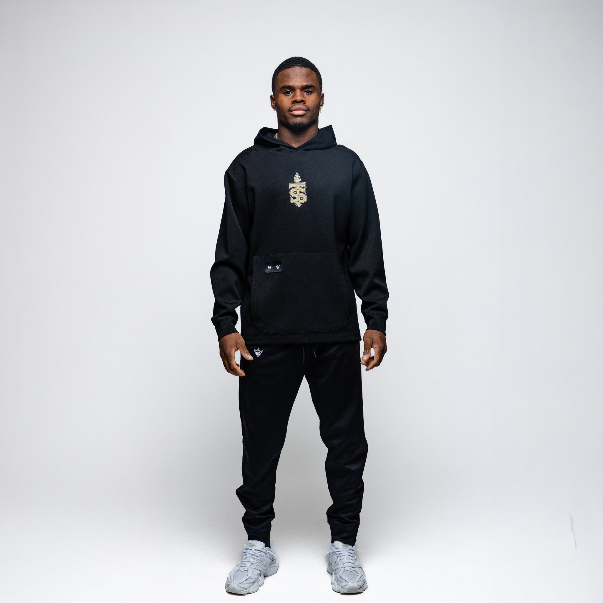 Man wearing a black hoodie and pants with a logo on a white background