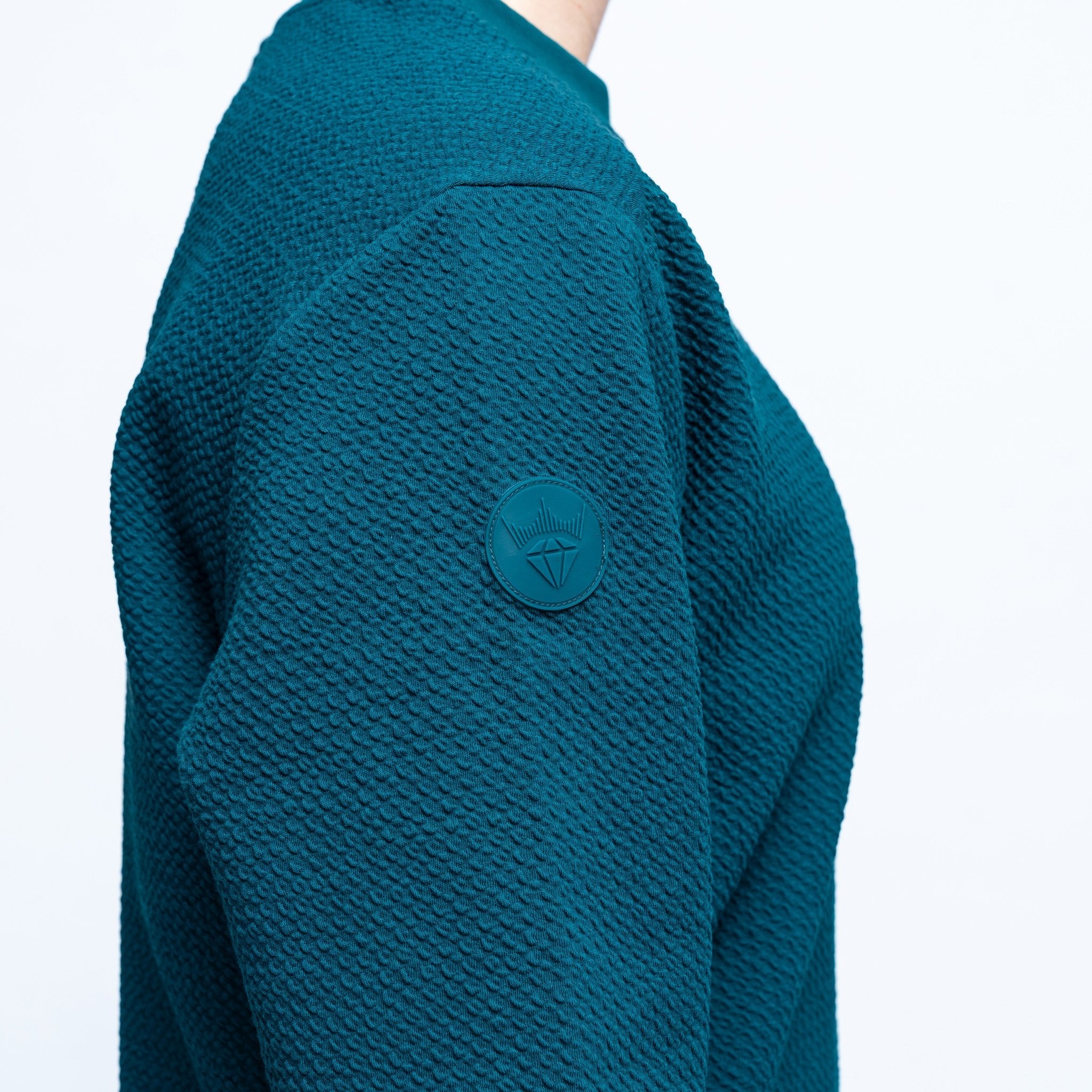 Teal textured sweater with a brand logo on a white background