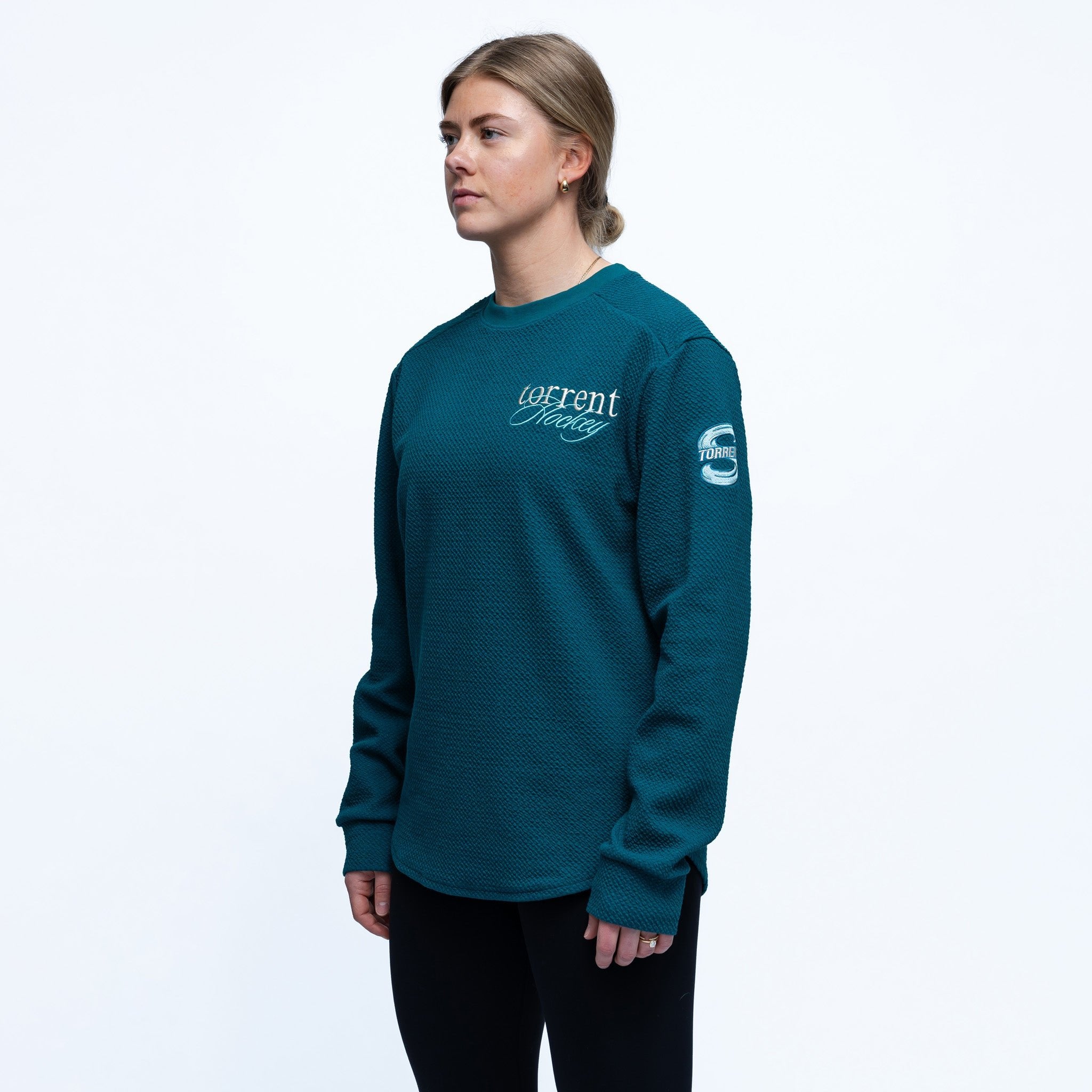 Person wearing a teal long-sleeve shirt with branding on a white background